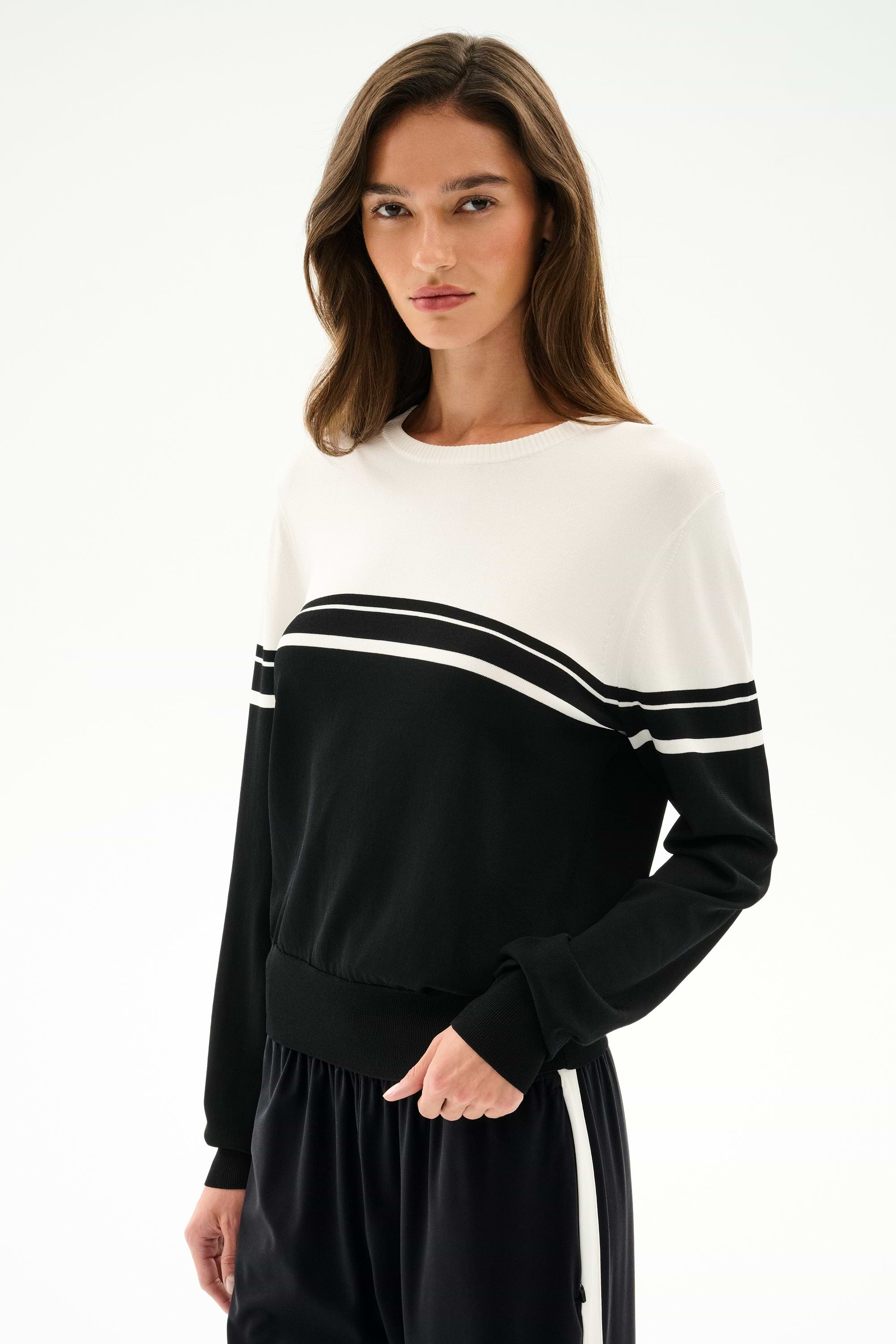 A woman models the Anna Knit Pullover - Black/White by SPLITS59, featuring black and white color-blocked stripes, against a plain white background.