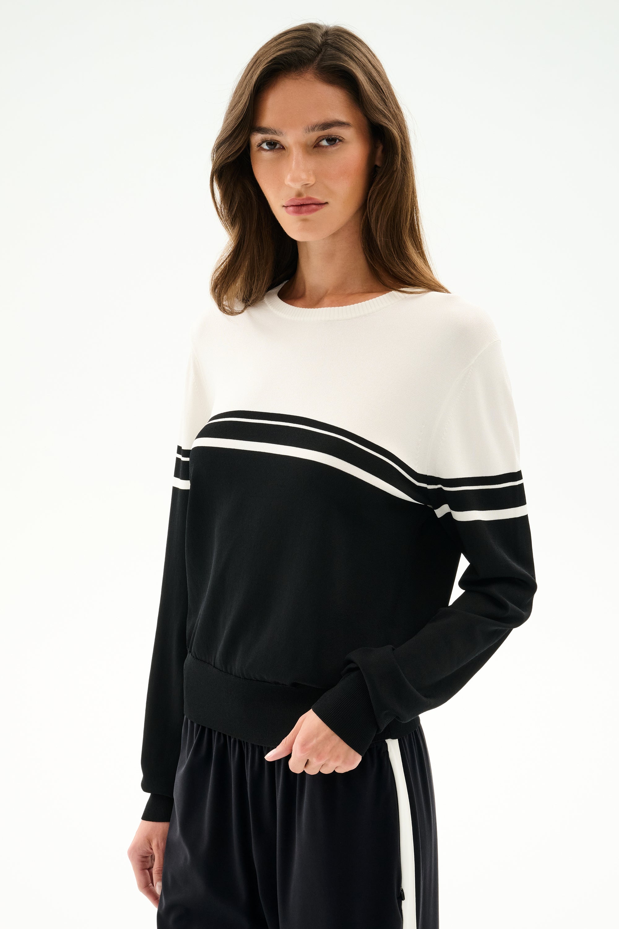 A woman models the Anna Knit Pullover - Black/White by SPLITS59, featuring black and white color-blocked stripes, against a plain white background.