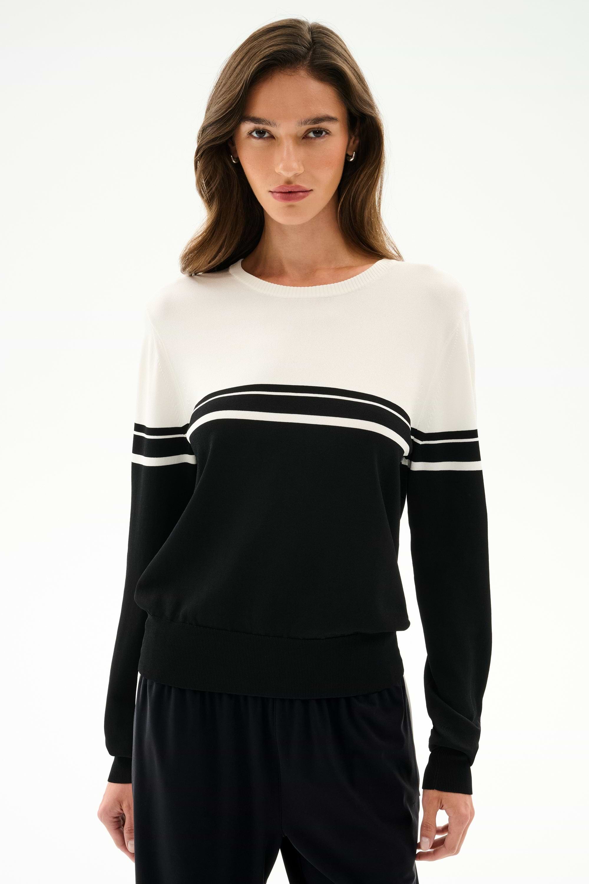 A woman wears the SPLITS59 Anna Knit Pullover - Black/White with black pants, standing against a plain light background.
