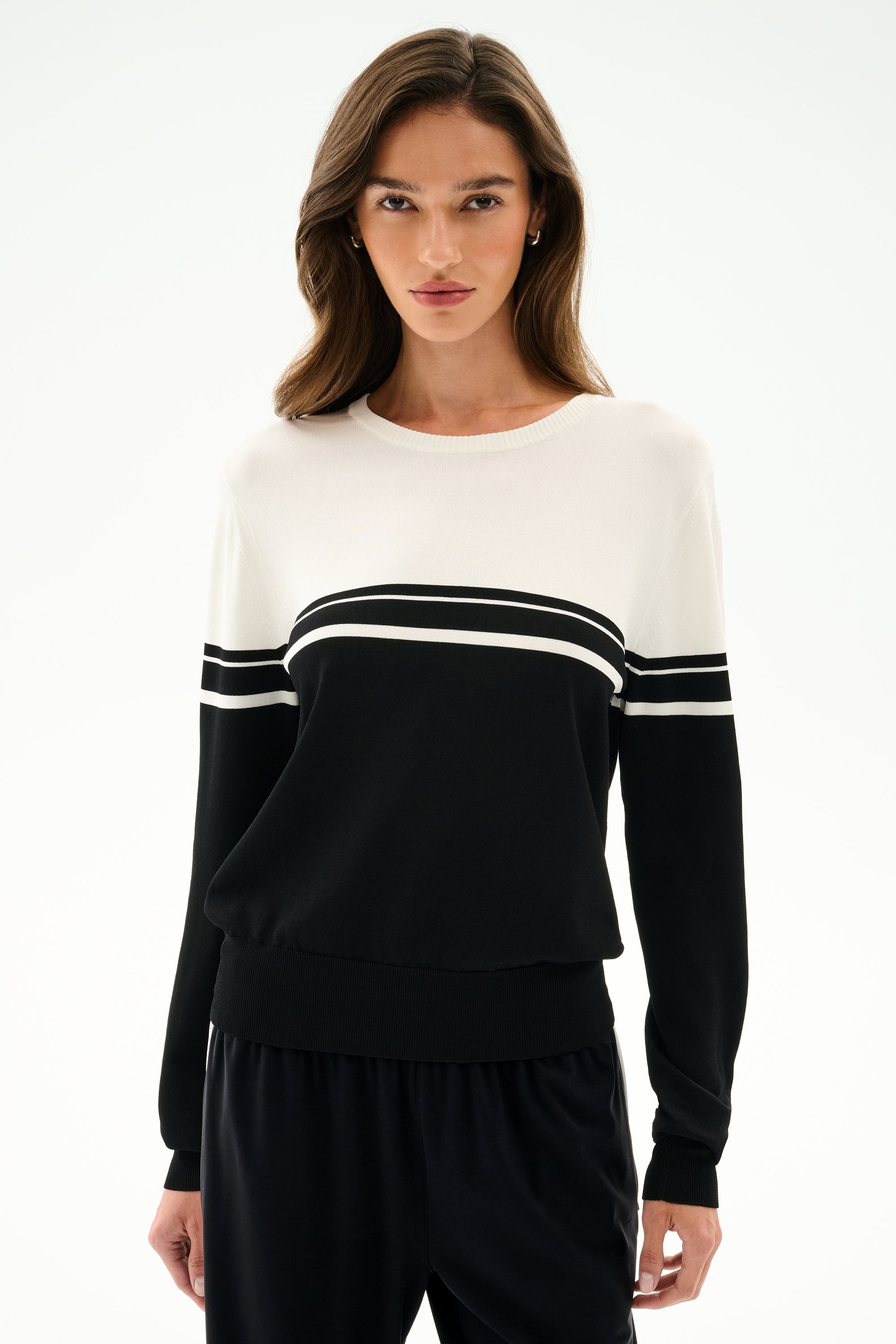 A woman wears the SPLITS59 Anna Knit Pullover - Black/White with black pants, standing against a plain light background.