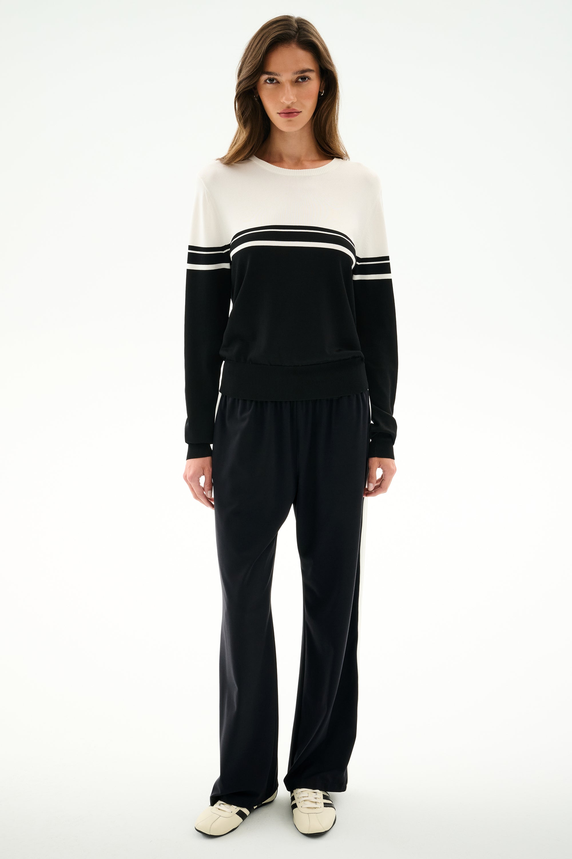 Woman standing against a white background, wearing the SPLITS59 Anna Knit Pullover - Black/White, black pants, and white sneakers.