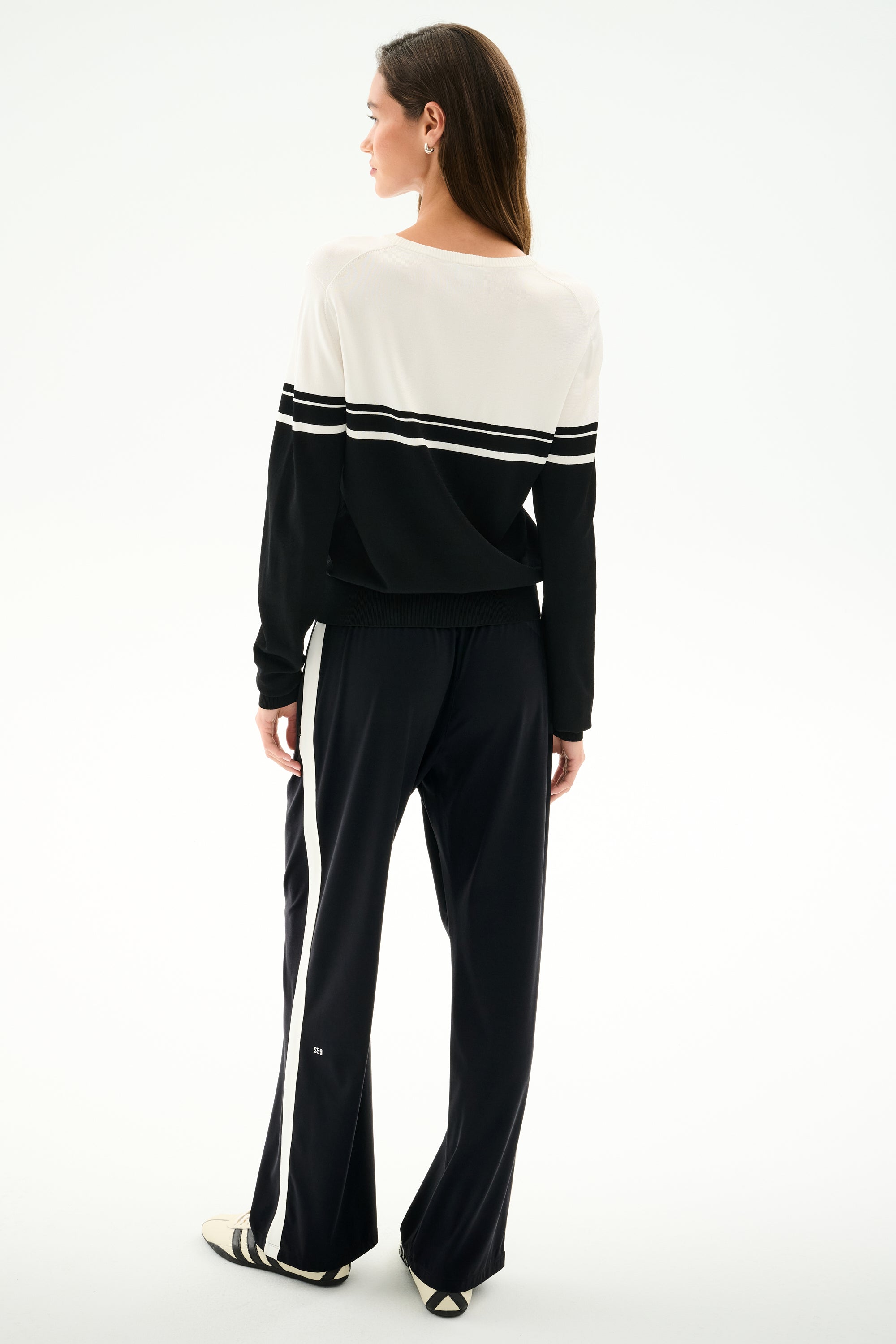 A woman faces away, wearing the SPLITS59 Anna Knit Pullover - Black/White with matching striped pants, both made of soft rayon fabric.