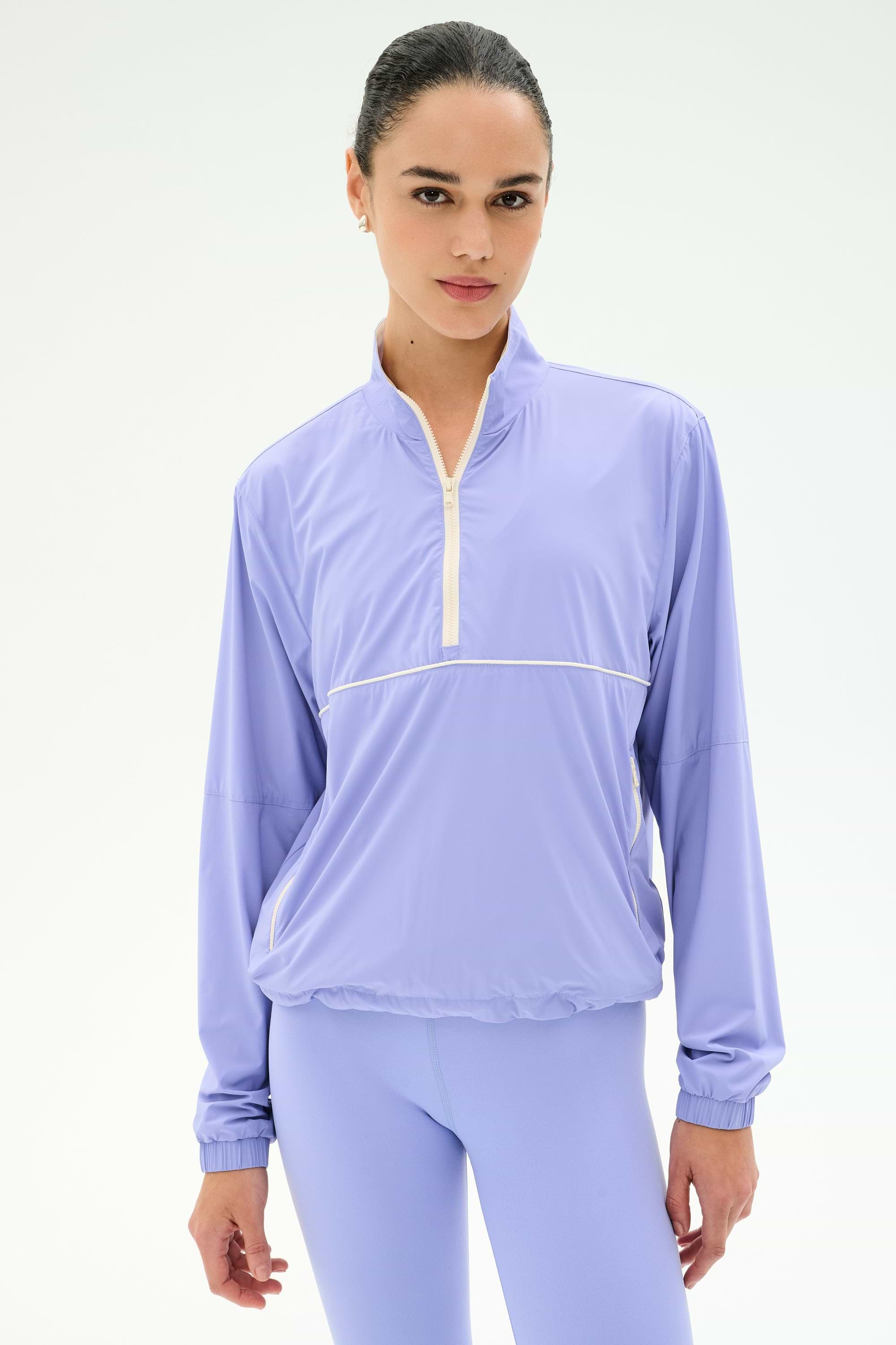 A woman wears the SPLITS59 Lyle Woven Nylon Pullover in Purple Haze/Creme, standing against a plain white background.