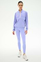 Someone stands facing forward against a white background, wearing the SPLITS59 Lyle Woven Nylon Pullover in Purple Haze/Creme, paired with matching spandex leggings and white sneakers.