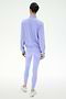 A person stands with their back to the camera, wearing the SPLITS59 Lyle Woven Nylon Pullover in Purple Haze/Creme and matching leggings with white sneakers against a plain white background.