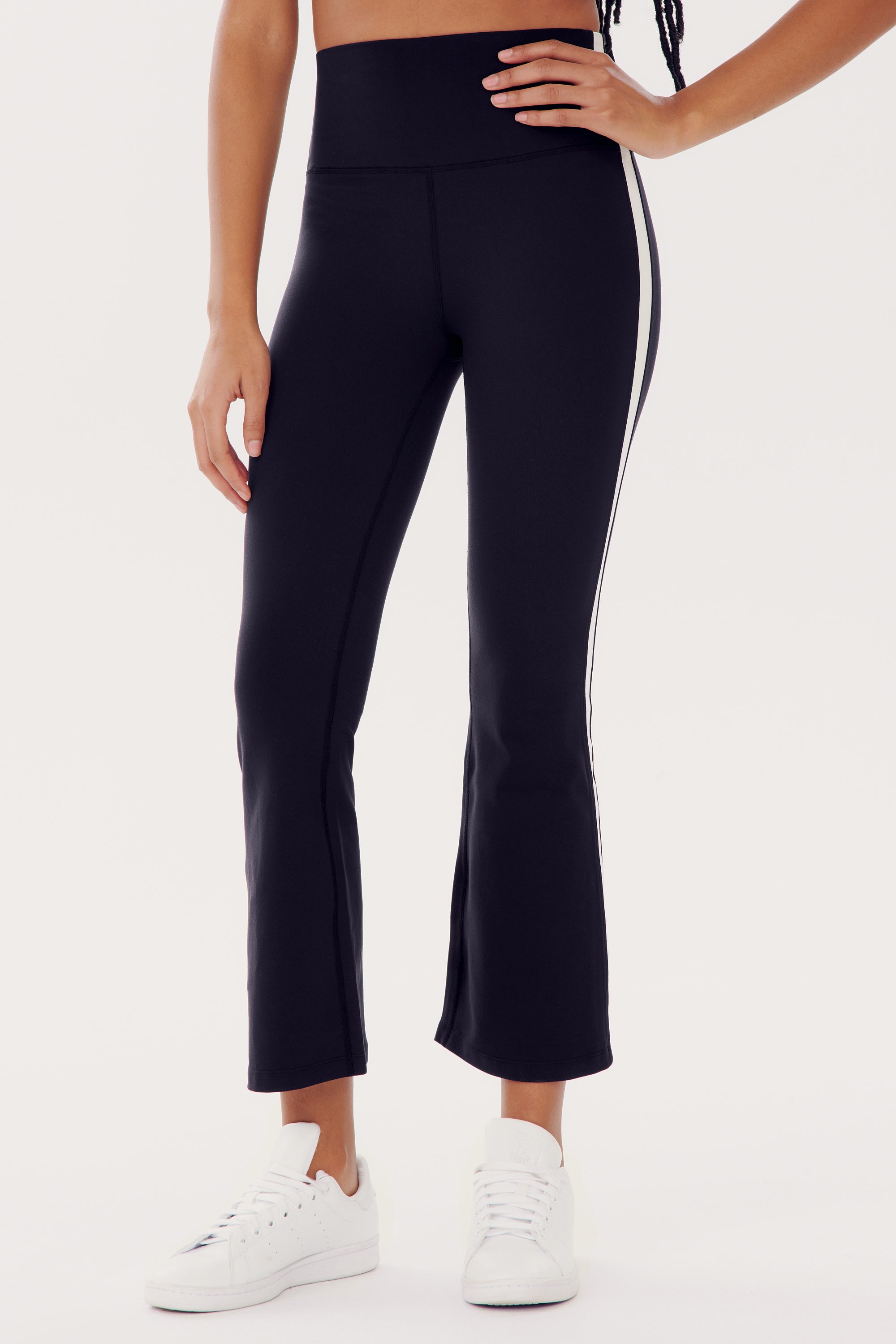 Person wearing SPLITS59 Raquel High Waist Crop - Black/White, made from 88% Nylon and Spandex blend, paired with white sneakers, standing against a plain white background.