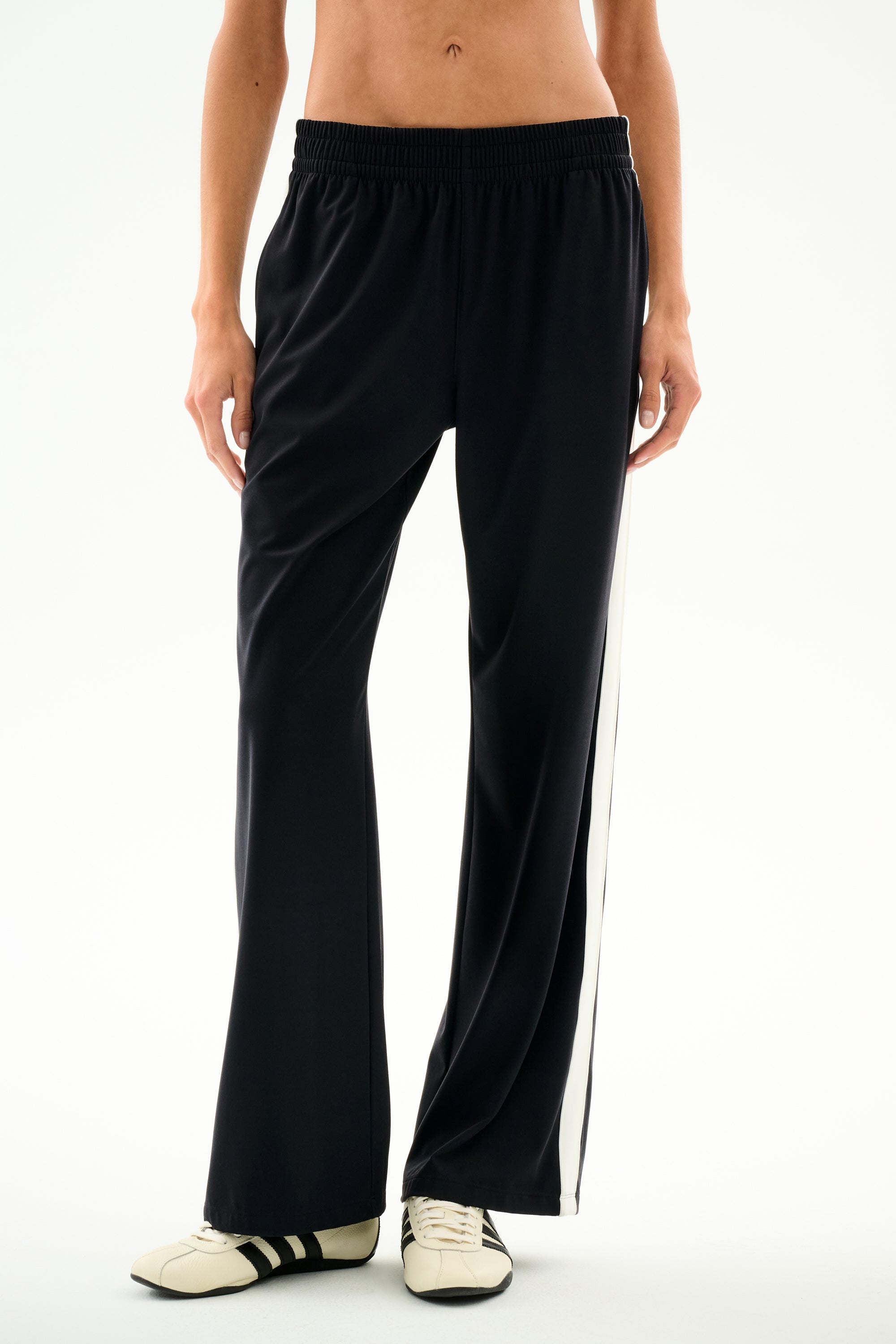 Black wide-leg Maxie Rigor Track Pant - Black/White with a white side stripe, worn with black and white sneakers.