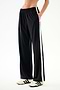 SPLITS59 Maxie Rigor Track Pant in black with a vertical white stripe down each side, worn with cream sneakers with black stripes.