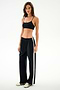 A woman wearing a black sports bra and wide-leg Maxie Rigor Track Pant - Black/White with white side stripes.