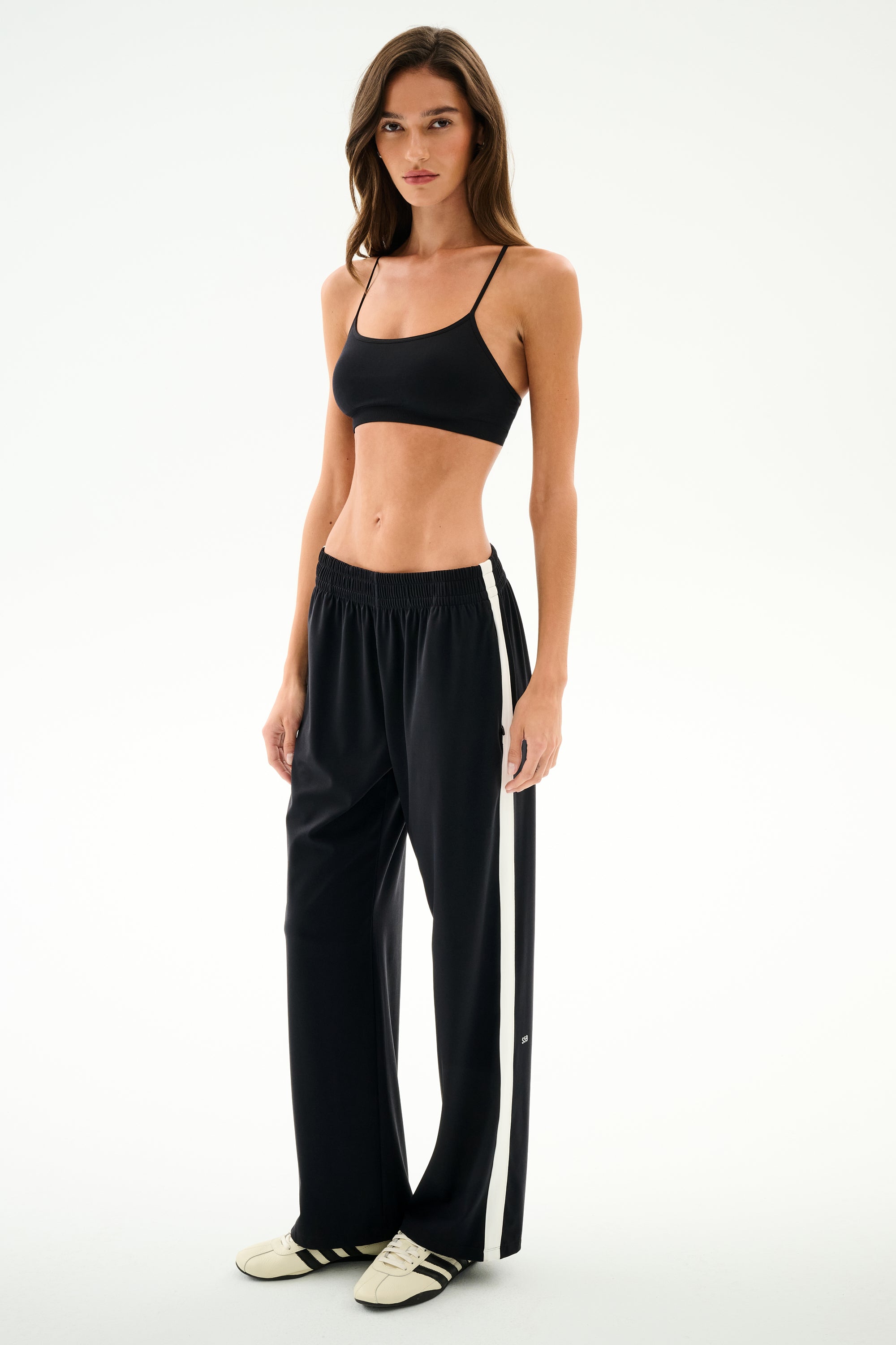 A woman wearing a black sports bra and wide-leg Maxie Rigor Track Pant - Black/White with white side stripes.