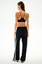A woman seen from behind wearing a black sports bra and Maxie Rigor Track Pant - Black/White with a white side stripe.