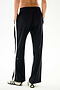 Rear view of a person wearing black and white Maxie Rigor Track Pants with wide legs, side stripes, and a small “59” logo on the lower leg.