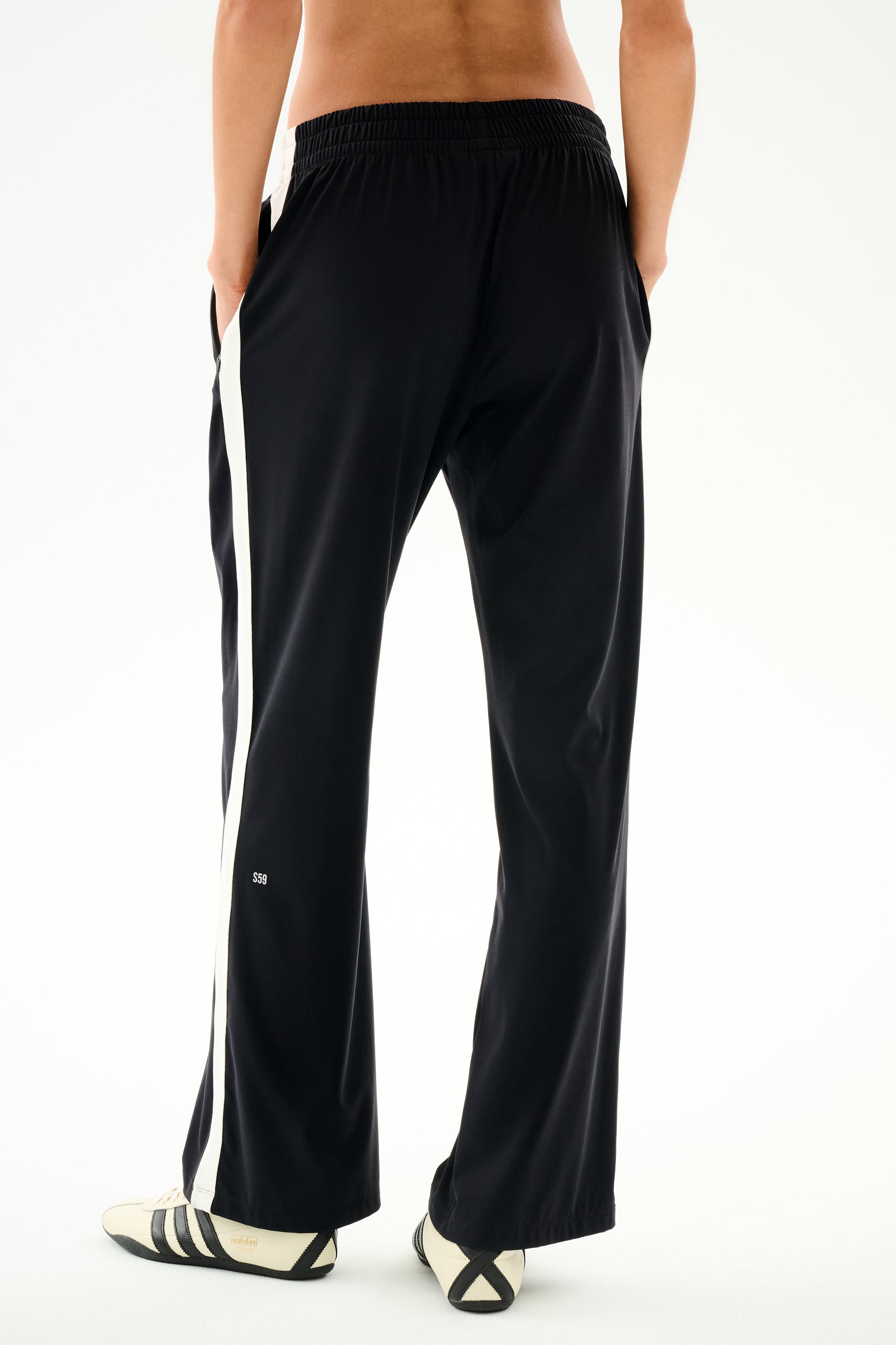 Rear view of a person wearing black and white Maxie Rigor Track Pants with wide legs, side stripes, and a small “59” logo on the lower leg.