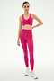 A person stands against a plain background wearing SPLITS59’s Airweight High Waist 26" leggings in Sangria with a matching sports bra and white athletic shoes.