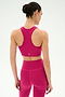 A woman faces away from the camera wearing the SPLITS59 Airweight Bra with Ruching in Sangria, paired with matching leggings, both crafted from stretch nylon spandex. She stands against a plain white background.