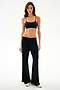 A woman stands against a white background wearing SPLITS59 Heritage Velour Pant - Black/Creme, a black crop top, and white shoes.