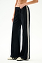 Person wearing SPLITS59 Heritage Velour Pant - Black/Creme with white stripes and cream sneakers, standing against a plain white background.