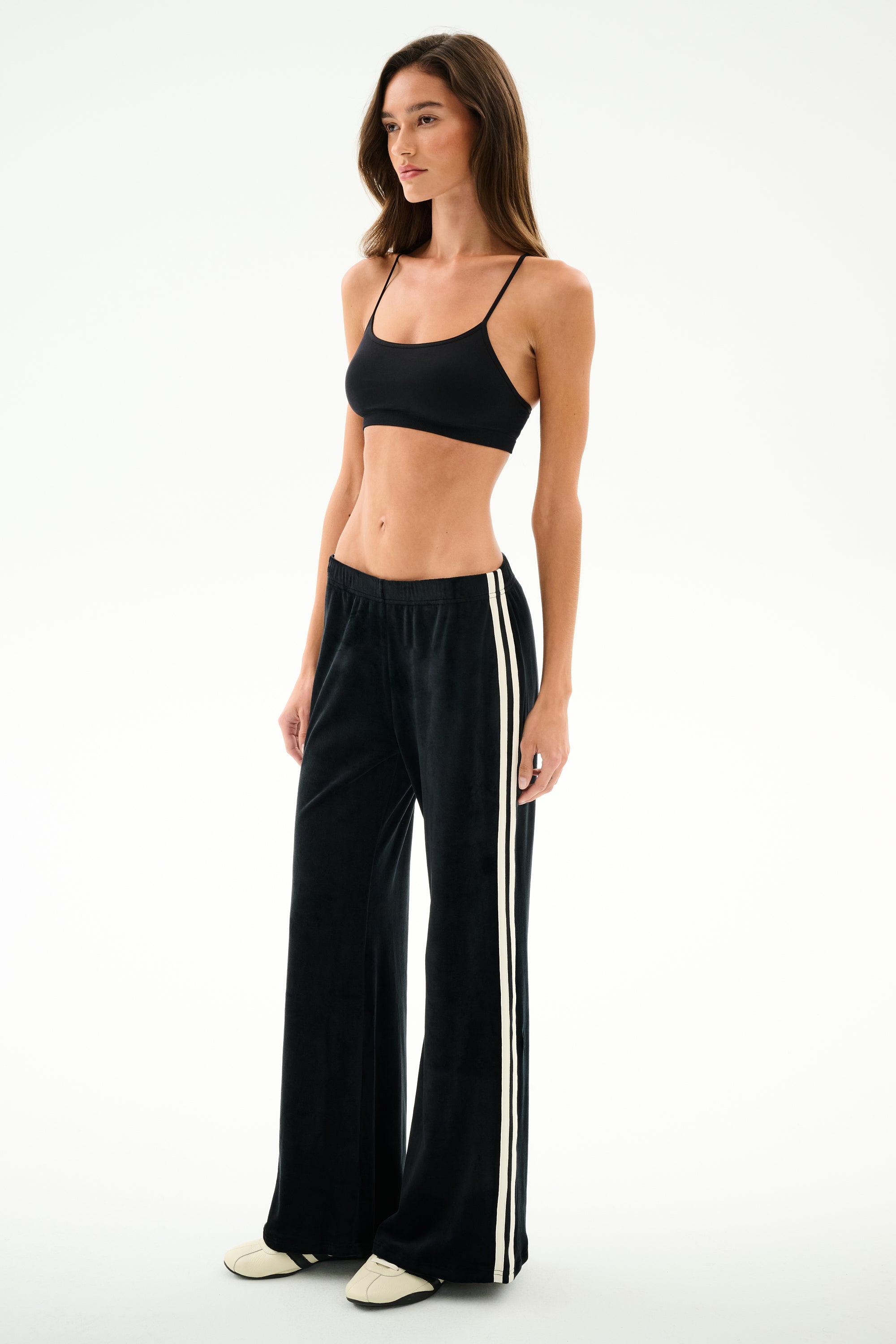 Woman wearing SPLITS59 Heritage Velour Pant - Black/Creme, featuring white side stripes, posed sideways against a plain white background.
