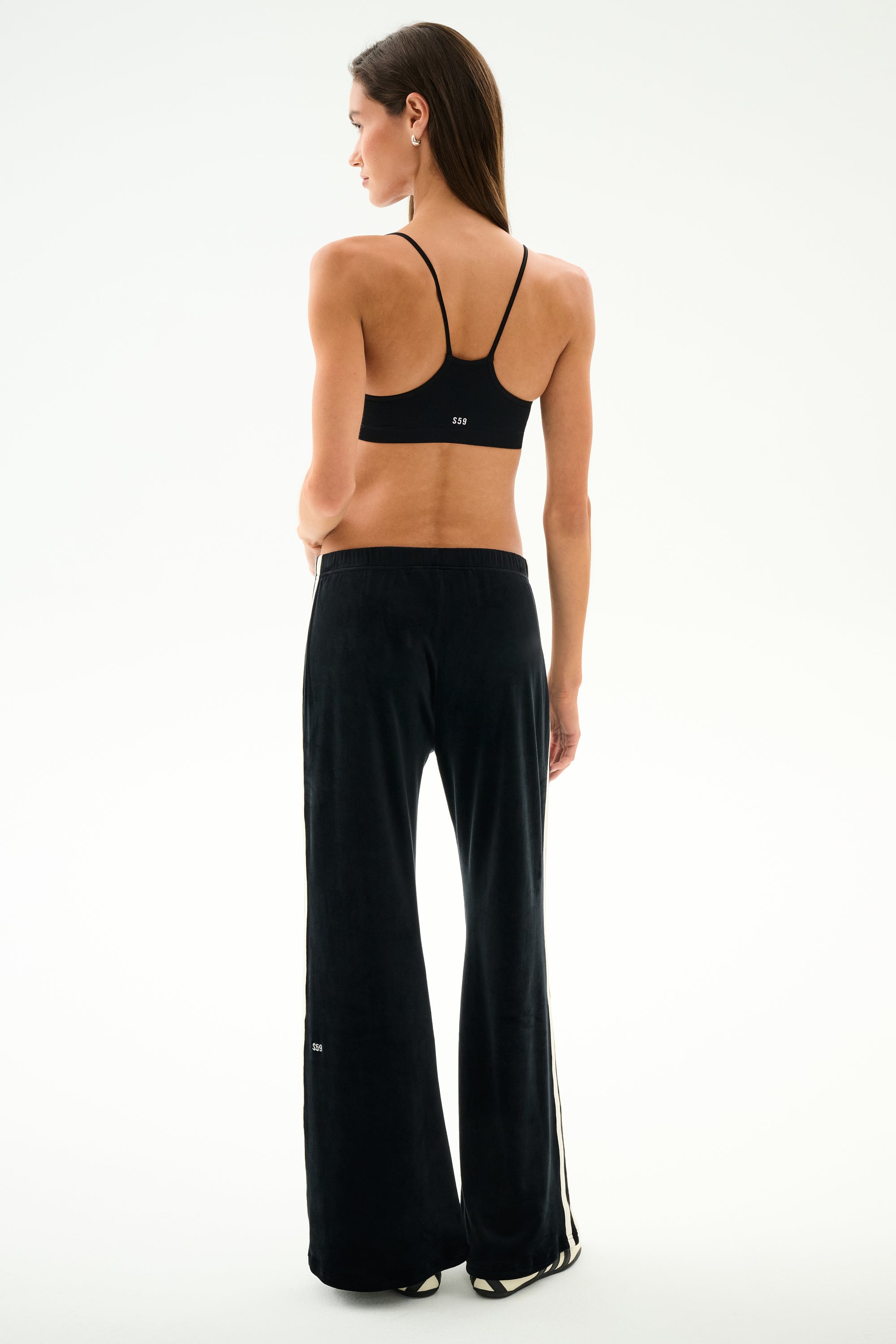 Woman stands with back to camera in black sports bra and SPLITS59 Heritage Velour Pant - Black/Creme, against a plain white background.