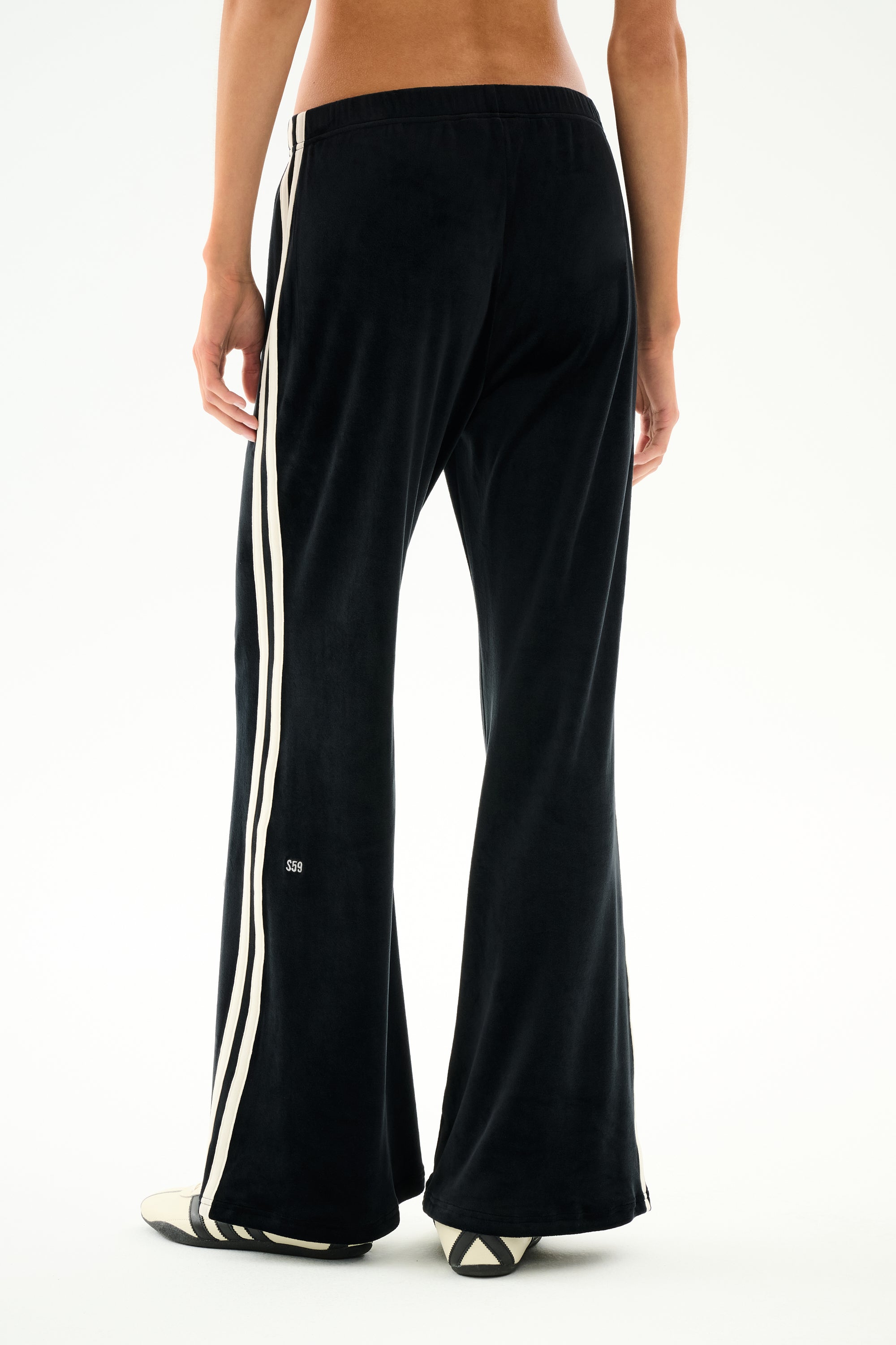 Person wearing SPLITS59 Heritage Velour Pant - Black/Creme, featuring white side stripes and stretch fabric, seen from the back on a white background.