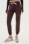 A person is wearing the Sonja Fleece Sweatpant - Dark Chocolate by SPLITS59, featuring a white drawstring, paired with beige sneakers. Perfect for cool weather workouts, the minimalistic backdrop is plain and white.