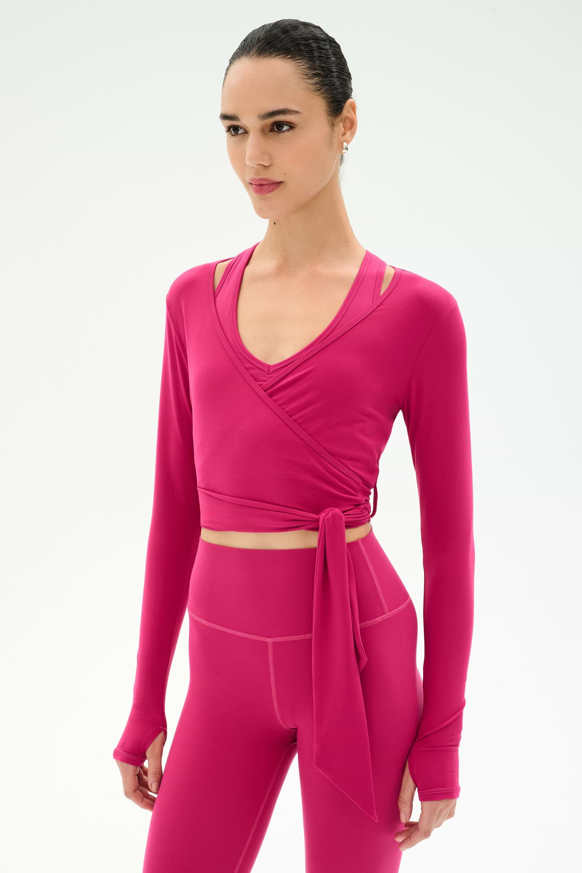 A woman wears the SPLITS59 Bella Airweight Lite Wrap in Sangria with matching high-waisted leggings, standing against a plain light background.