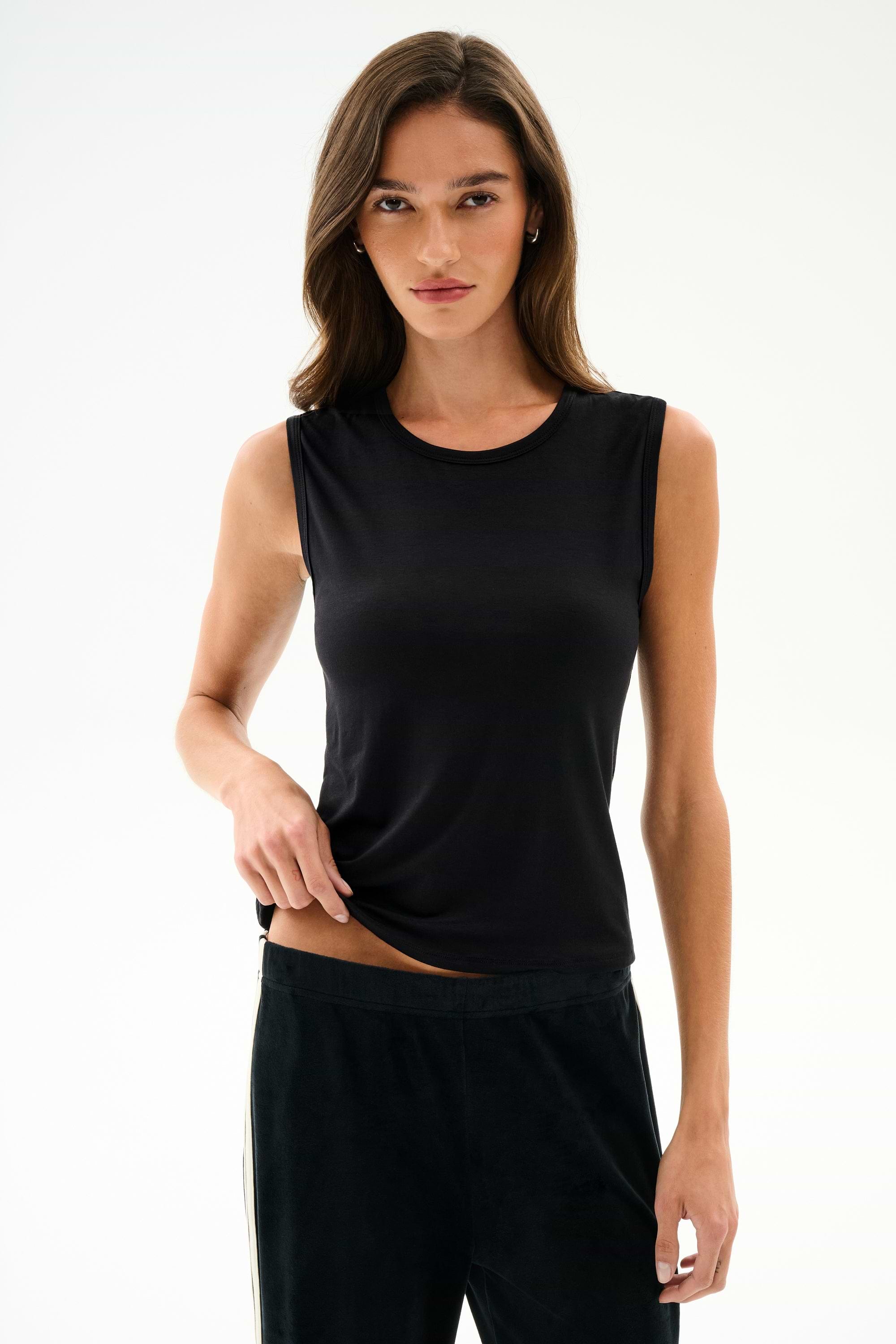 Model wearing SPLITS59 Nikki Jersey Tank - Black and dark pants stands against a white background, facing the camera.