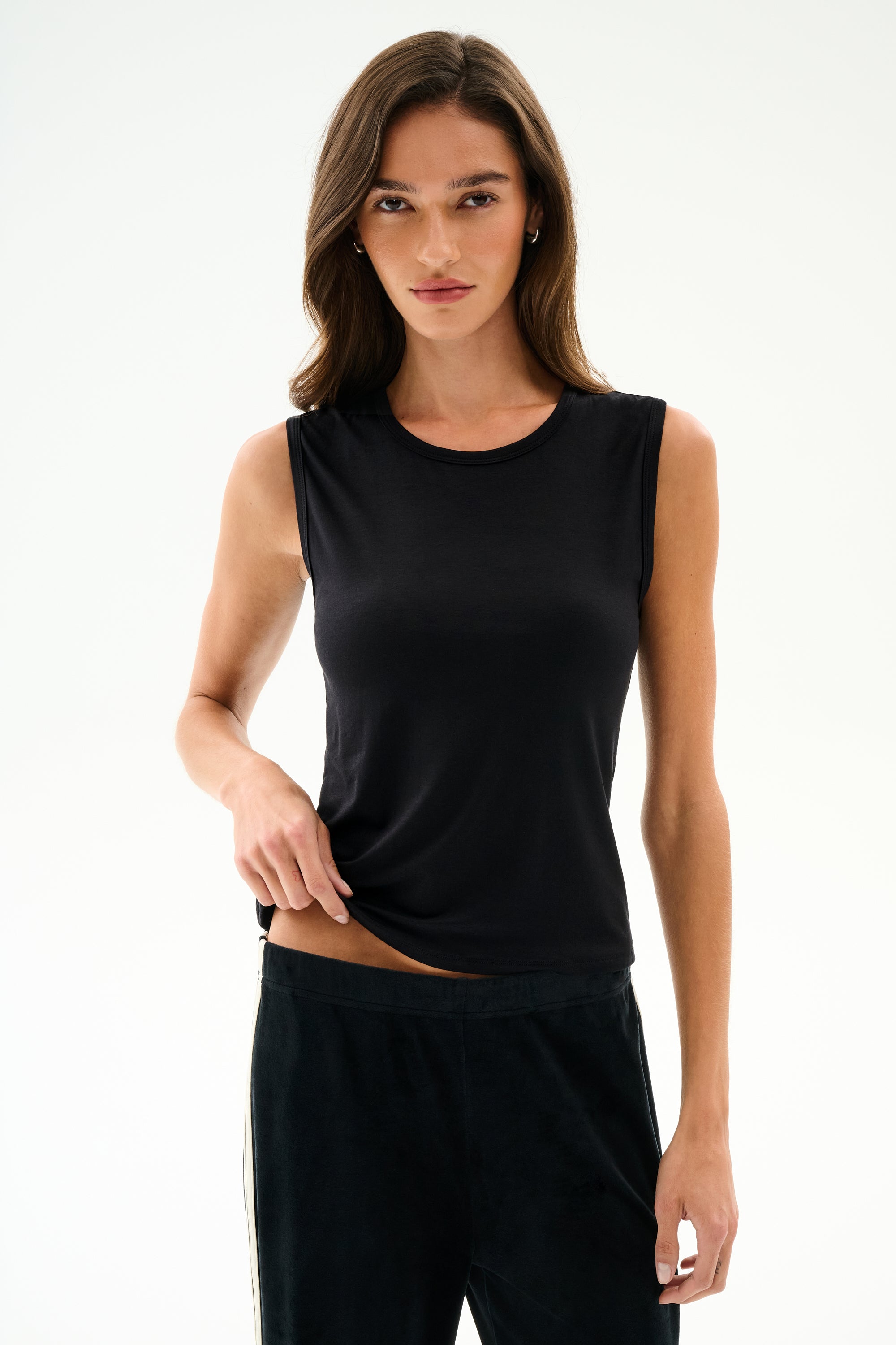 Model wearing SPLITS59 Nikki Jersey Tank - Black and dark pants stands against a white background, facing the camera.