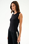 A woman wears the SPLITS59 Nikki Jersey Tank - Black with black pants featuring white stripes, standing against a plain light background, facing forward neutrally.