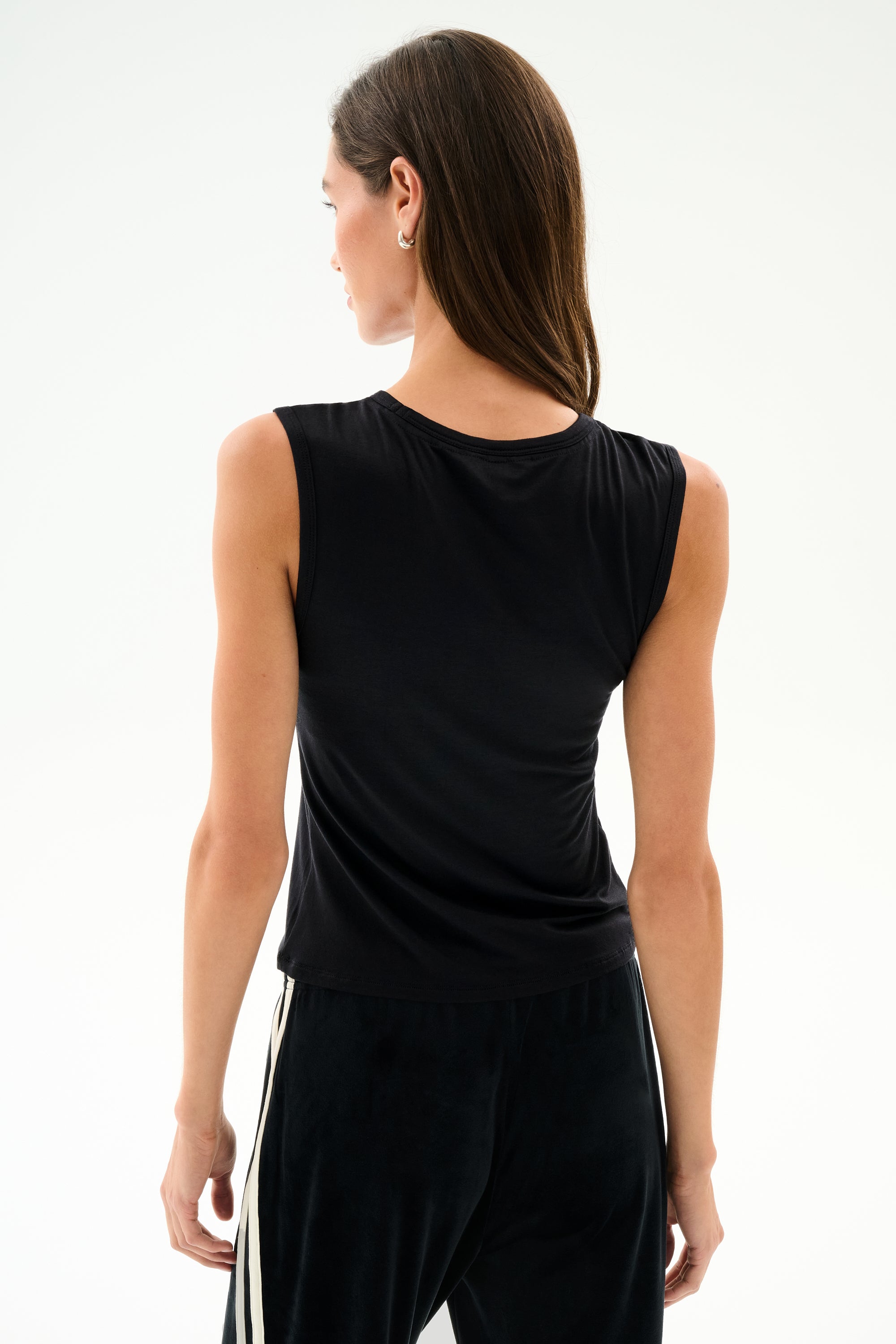 Woman with her back to the camera wears the SPLITS59 Nikki Jersey Tank - Black and black pants with white side stripes, set against a plain white background.
