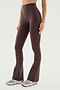 A person wears SPLITS59 Raquel High Waist Flared Legging in Dark Chocolate, featuring 4-way stretch, and white sneakers, standing against a plain white background.