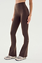 A person wears SPLITS59 Raquel High Waist Flared Legging in Dark Chocolate, featuring 4-way stretch, and white sneakers, standing against a plain white background.