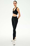 A person stands in a studio wearing SPLITS59 Airweight High Waist Legging in black—ideal for hot yoga—paired with a black sports bra and white athletic shoes, arms behind their back.