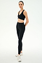 A person stands in a studio wearing SPLITS59 Airweight High Waist Legging in black—ideal for hot yoga—paired with a black sports bra and white athletic shoes, arms behind their back.