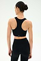 A woman faces away in the SPLITS59 Airweight Bra with Ruching - Black, paired with black high-waisted leggings against a plain light background—ideal for hot yoga sessions.