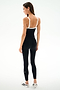 A woman stands facing away in the SPLITS59 Monah Rigor Jumpsuit 7/8 - Black/White with white sneakers, set against a plain white background.