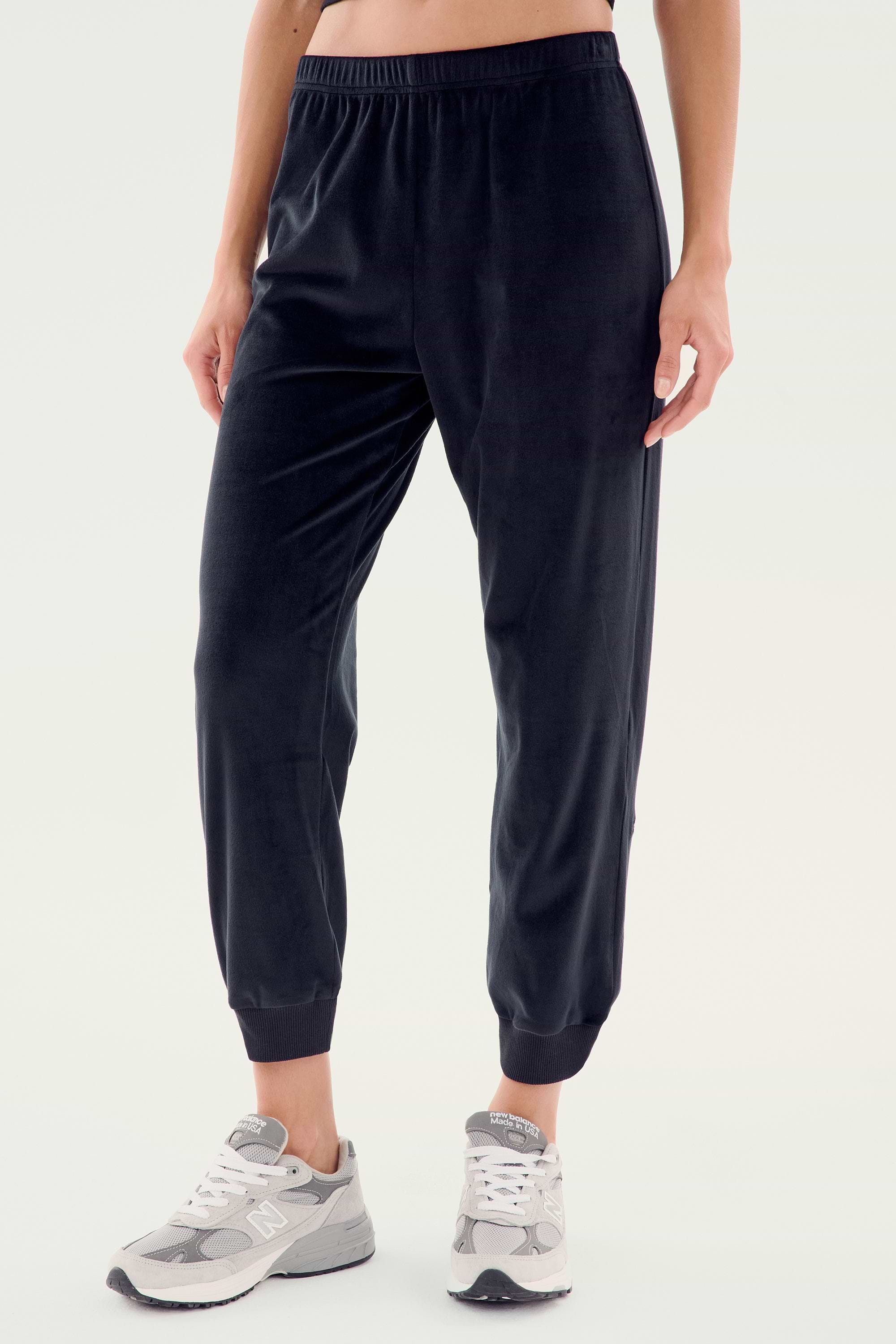 Person wearing black SPLITS59 Rhys Velour Jogger pants and gray sneakers, standing against a plain light background. Upper body is not visible, exemplifying effortless casual wear and ultimate comfort.