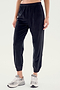 Person wearing black SPLITS59 Rhys Velour Jogger pants and gray sneakers, standing against a plain light background. Upper body is not visible, exemplifying effortless casual wear and ultimate comfort.