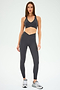 A woman stands on a white background wearing the SPLITS59 Mia Rigor Bra in Graphite, paired with matching high-waisted leggings and gray sneakers—an outfit designed for multi-sport performance and ideal for gym workouts.