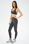 A woman stands in a neutral pose against a plain white background, wearing the SPLITS59 Mia Rigor Bra in Graphite paired with matching leggings and gray sneakers—an ideal outfit for multi-sport performance.