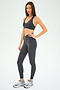 A woman stands in a neutral pose against a plain white background, wearing the SPLITS59 Mia Rigor Bra in Graphite paired with matching leggings and gray sneakers—an ideal outfit for multi-sport performance.