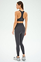 A woman, viewed from the back against a white background, wears the SPLITS59 Mia Rigor 7/8 - Graphite high waist leggings crafted from Rigor fabric for superior support, paired with a black sports bra and gray athletic shoes.