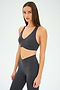 Wearing the SPLITS59 Mia Rigor Bra in Graphite and matching high-waisted leggings, a woman stands against a plain white background, showcasing an outfit designed for multi-sport performance.