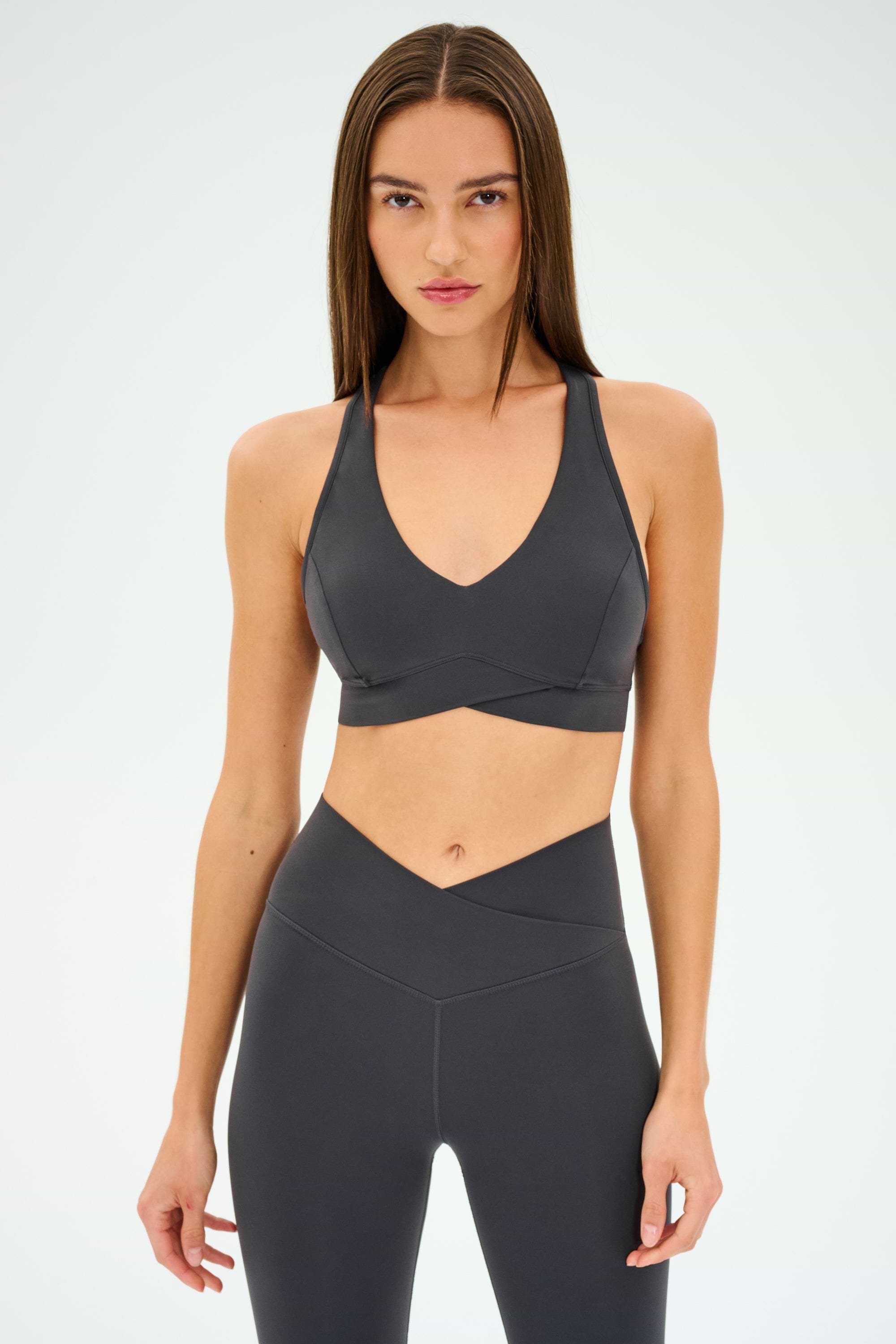 A woman stands facing forward against a plain white background, wearing the SPLITS59 Mia Rigor Bra in Graphite paired with matching high-waisted leggings, both designed for multisport performance.