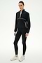 A woman wears the SPLITS59 Lyle Woven Nylon Pullover in Black/Creme, styled with spandex leggings and white sneakers, standing against a plain white background.