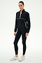 A woman wears the SPLITS59 Lyle Woven Nylon Pullover in Black/Creme, styled with spandex leggings and white sneakers, standing against a plain white background.