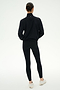 A person stands with their back to the camera, wearing the SPLITS59 Lyle Woven Nylon Pullover in Black/Creme, paired with black spandex leggings and white sneakers against a plain light background.
