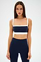 Against a plain background, a person in an indigo and white athletic outfit exudes a retro sport vibe, featuring the SPLITS59 Monah Rigor Bra for solid support.
