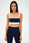 Against a plain background, a person in an indigo and white athletic outfit exudes a retro sport vibe, featuring the SPLITS59 Monah Rigor Bra for solid support.