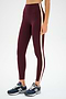 A person stands against a white background wearing SPLITS59 Clare High Waist Rigor 7/8 leggings in Dark Cherry/Creme with maroon Rigor fabric and beige side stripe, paired with dark blue New Balance sneakers.